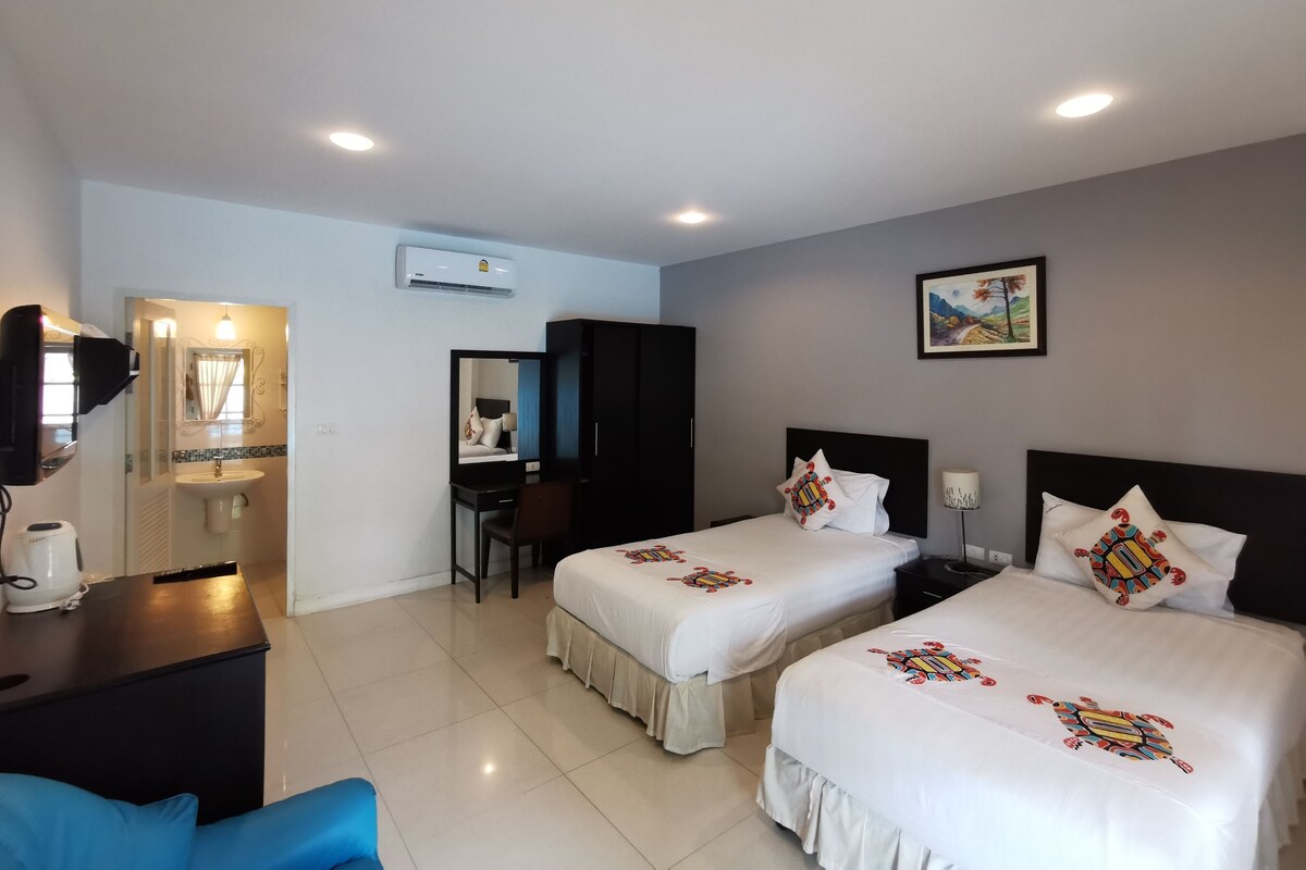 A hotel room with two beds, a desk, a chair, a mirror, a sink, and an air conditioning unit.