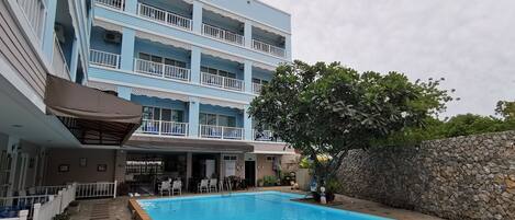 A pool area with a stone wall and a building with balconies in the background.