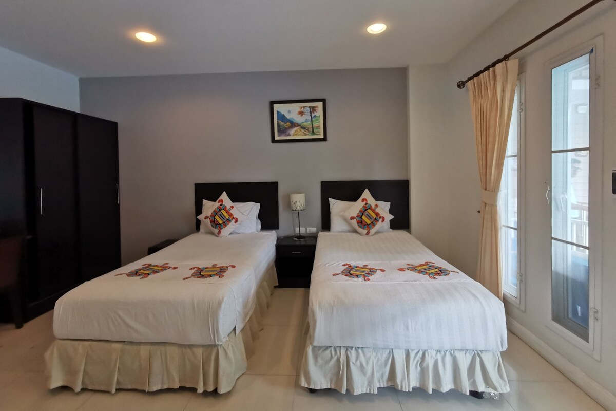 Habitación de hotel con dos camas, un armario, una mesita de noche, una lámpara y una ventana con cortinas.