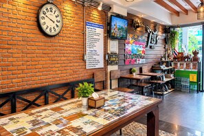 Interior de un restaurante con pared de ladrillo, un reloj, una pizarra de menú y un televisor.