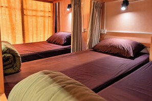 A room with two single beds, each with a pillow and a blanket. There is a window with curtains, a wall-mounted light, and a power outlet. - T2B Hostel (Chiang Mai)