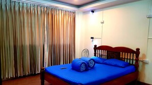 A bedroom with a wooden bed, blue bedding, and a curtain-covered window. - T2B Home - Hostel (Chiang Mai)
