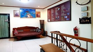 A hotel lobby with a wooden sofa, a staircase, and a wall with informational signs. - T2B Home - Hostel (Chiang Mai)