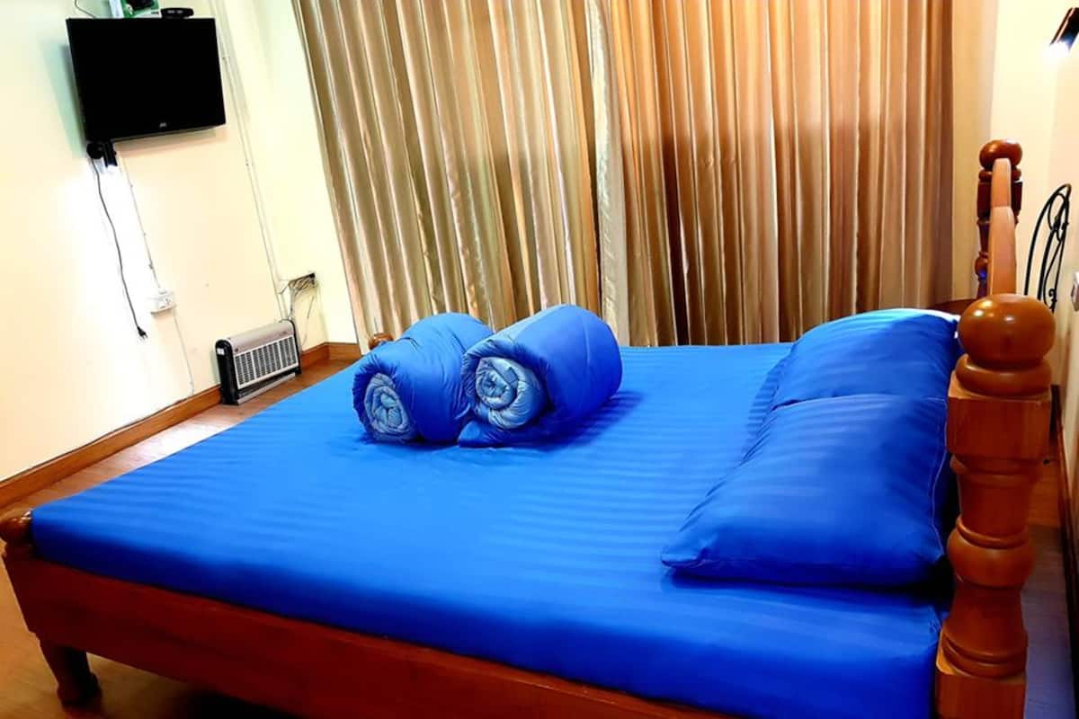 A bed with blue bedding, a wooden headboard, and a wall-mounted TV.