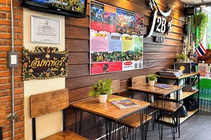A restaurant interior with wooden tables and chairs, a wall-mounted menu, and a sign indicating the restaurant's name. - T2B Hostel (Chiang Mai)