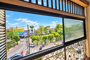 Vista desde una ventana con baranda de metal, con vista a una calle con vehículos y vegetación.