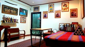 A room with a bed, a desk, a chair, and a bench. There are framed pictures on the walls. - T2B Home - Hostel (Chiang Mai)