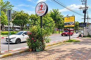 A hostel sign with a contact number, a Vienna de Cafe sign, and a red vehicle on the road. - T2B Hostel (Chiang Mai)