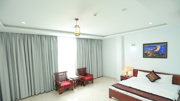Habitación de hotel con una cama grande, dos sillones, una mesita, una mesita de noche con lámpara y un cuadro en la pared.