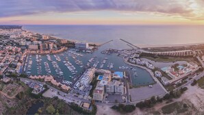 An aerial view of a coastal marina with numerous boats docked, connected piers, and a mix of residential and commercial buildings. - Luxury Villa Jose with swimming pool (Quarteira)