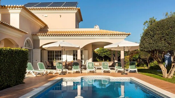A swimming pool with lounge chairs and umbrellas, surrounded by a building with a tiled roof and a pergola. - Luxury Villa Jose with swimming pool (Quarteira)