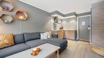 Una sala moderna con un sofá gris, una mesa de centro blanca y una cocina con armarios de madera y horno empotrado.