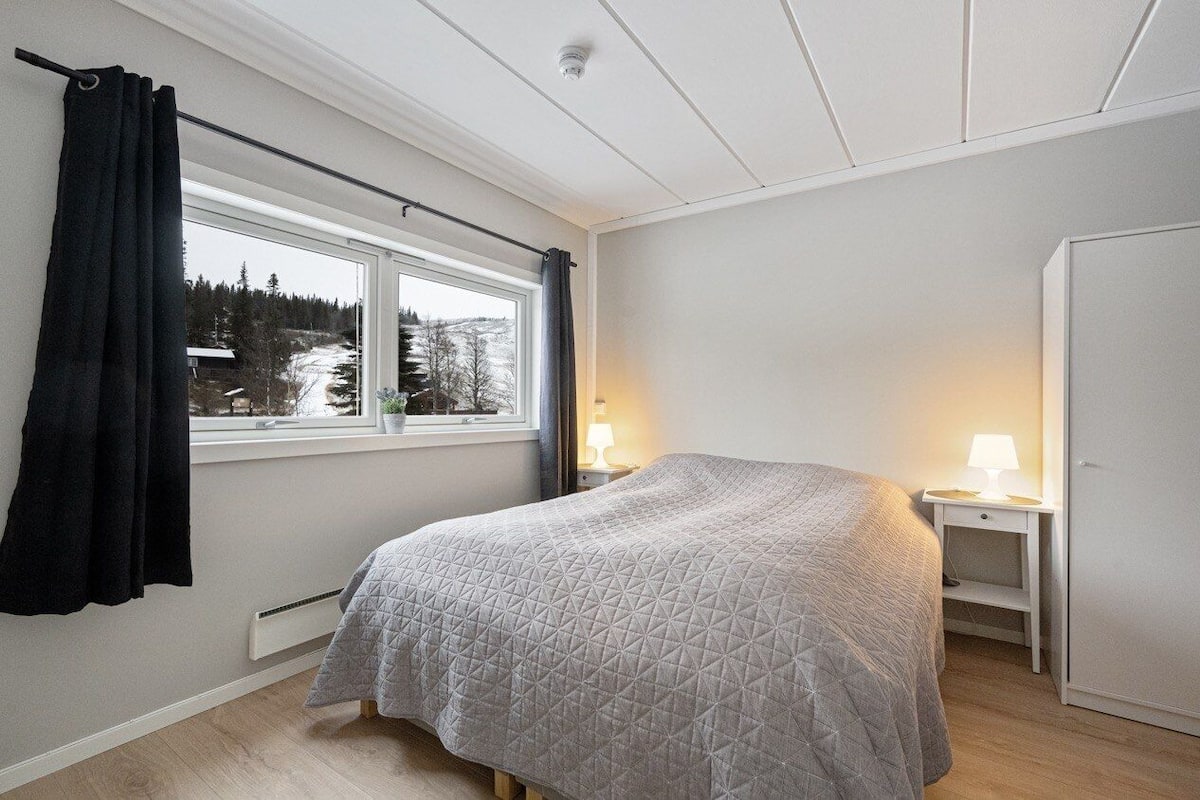 Une chambre à coucher avec un lit, une fenêtre avec des rideaux, une table de chevet avec une lampe et une armoire.