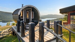 A wooden deck leading to a cabin with a large window and a door, overlooking a lake and mountains. - Spåtind Fjellhotell (Nordre Land)