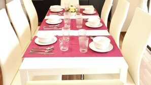 Un comedor con una mesa larga dispuesta para cuatro, sillas blancas y un mantel rojo.