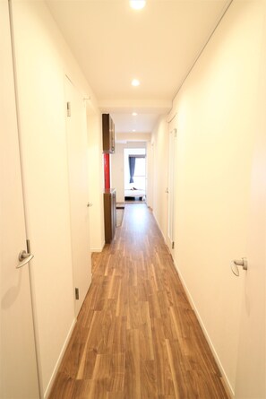 A narrow hallway with wooden flooring, white walls, and a door on the left. - ABC Nishigokencho (Tokyo)