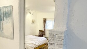 A bedroom with a bed, a wooden chair, a window with curtains, and a white wall with a textured section. - Gallery Hara & Guest House (Hara)
