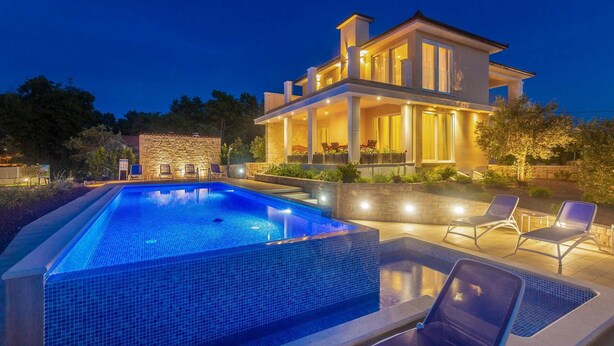 A modern two-story house with a swimming pool, outdoor seating, and a stone wall.