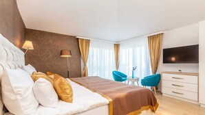A modern hotel room with a large bed, a desk, two chairs, a TV, and a window with curtains.