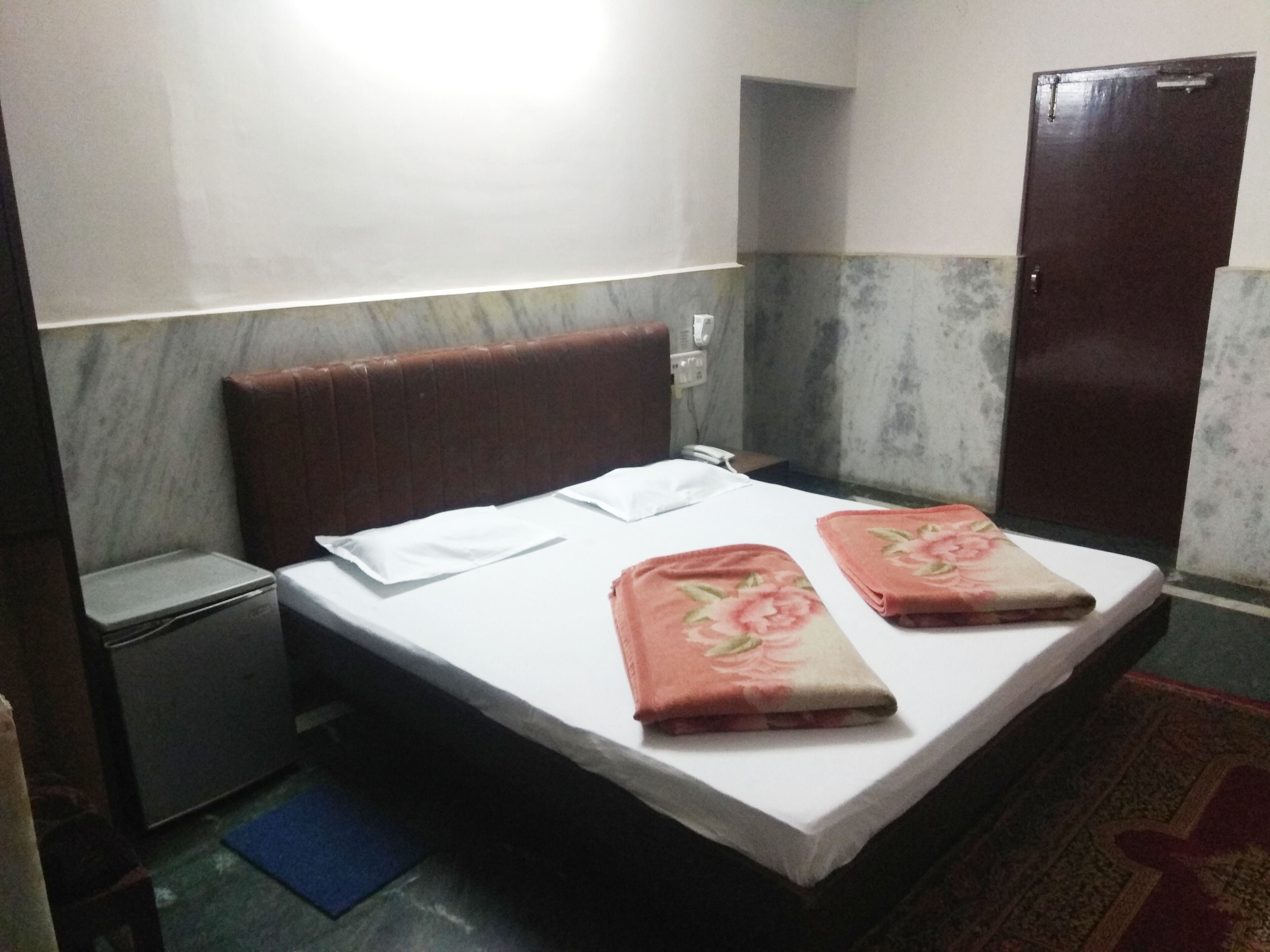 A small, simple room with a bed, a nightstand, a wardrobe, and a blue mat on the floor.