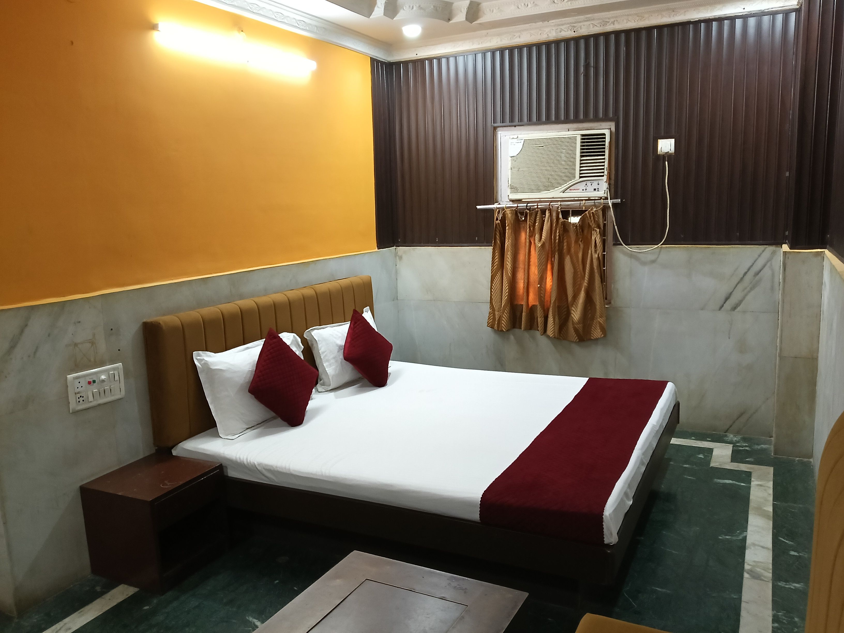 Habitación de hotel con cama, mesita de noche, aire acondicionado instalado en la pared y un enchufe.