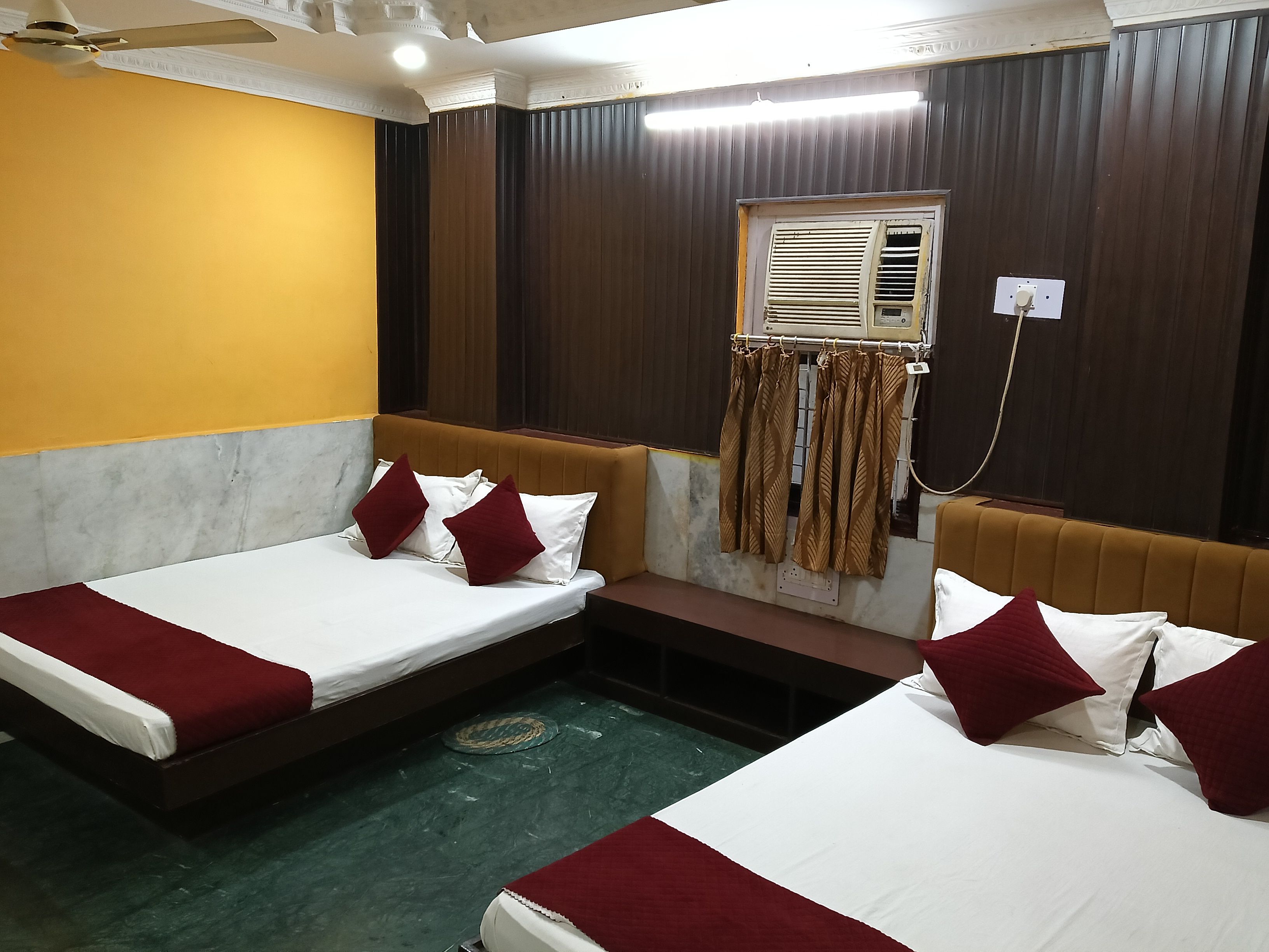A hotel room with two beds, a bench, a window with curtains, and a ceiling fan.