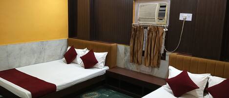 A hotel room with two beds, a bench, a window with curtains, and a ceiling fan.