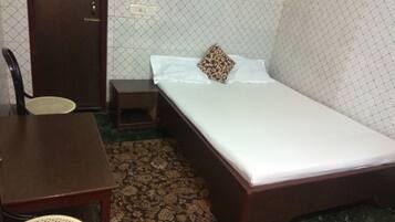 A small, neatly arranged room with a single bed, a wooden nightstand, a chair, and a small table.
