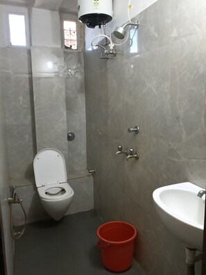 A bathroom with a toilet, bidet, sink, and a red bucket on the floor. - Hotel Prince (Guwahati)