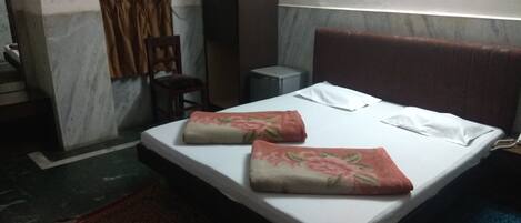 A hotel room with a bed, a chair, a small table, and an air conditioning unit.