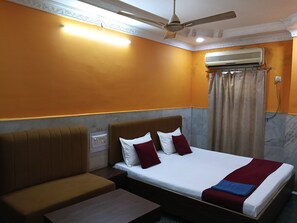 A hotel room with a bed, a sofa, a ceiling fan, an air conditioning unit, and a power outlet.
