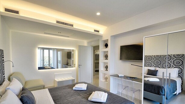 A modern hotel room with a large bed, a desk, a mirror, and a wardrobe.