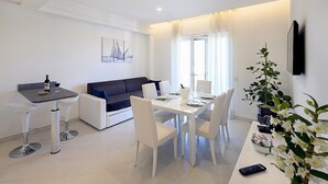 A modern living room with a dining area, a sofa, a coffee table, and a TV mounted on the wall.