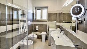 A modern bathroom with a glass shower enclosure, a double sink vanity, a toilet, and a window providing natural light.