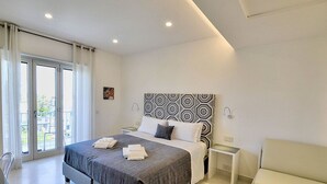 A modern hotel room with a large bed, a bedside table, a chair, and a view of the outdoors through a sliding door.