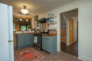 A kitchen with teal cabinetry, a stove, a microwave, and a hanging light fixture.