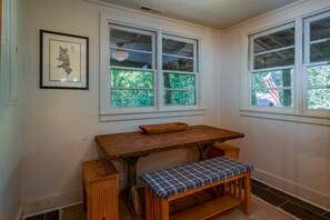 A corner room with a wooden table and bench, two windows with views of greenery, and a framed picture on the wall. - Horseshoe Hollow, Private Log Cabin on 10 acres (Lake Toxaway)