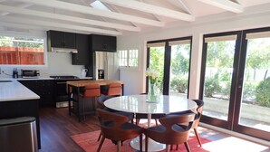 A modern kitchen with dark cabinets, a microwave, and a stove. There is a dining area with a round table and chairs, and a red rug on the floor. - Gorgeous 2Bd + Loft with Deck and Gardens. Soaring 20 ft ceilings, huge windows! (Kentfield)