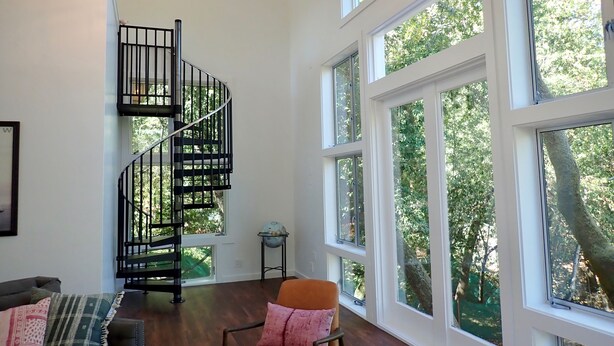 A spacious living area with a spiral staircase, large windows, and a view of greenery outside. - Gorgeous 2Bd + Loft with Deck and Gardens. Soaring 20 ft ceilings, huge windows! (Kentfield)