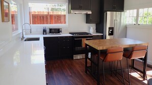 A compact kitchen with a wooden table, two bar stools, a microwave, a stove, and a refrigerator. - Gorgeous 2Bd + Loft with Deck and Gardens. Soaring 20 ft ceilings, huge windows! (Kentfield)