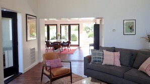 A spacious living area with a grey sofa, a brown leather chair, and a dining table with chairs. - Gorgeous 2Bd + Loft with Deck and Gardens. Soaring 20 ft ceilings, huge windows! (Kentfield)