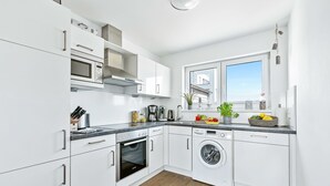 Eine moderne Küche mit weißen Schränken, einem Einbauofen, einer Mikrowelle, einer Kaffeemaschine und einer Waschmaschine.
