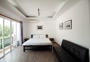 A bedroom with a bed, a black sofa, and a balcony with a view.