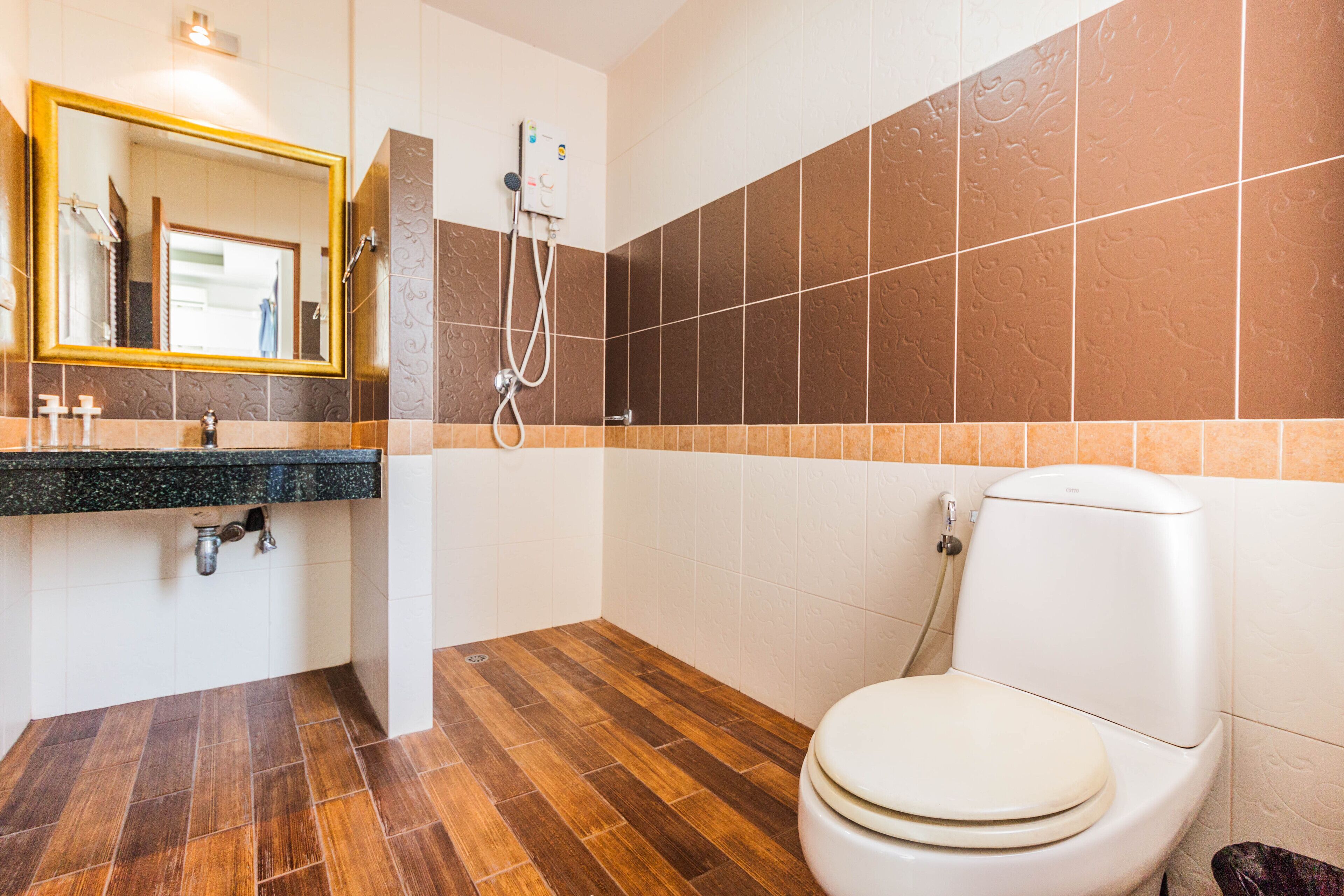 A bathroom with a wooden floor, a white toilet, a sink with a mirror, and a shower with a control panel.