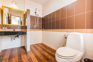 A bathroom with a wooden floor, a white toilet, a sink with a mirror, and a shower with a control panel.