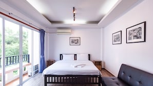 Quarto com cama grande, sofá escuro e varanda com vista para o verde.