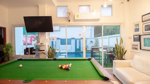 Uma mesa de bilhar com bolas, uma televisão em cima e vista para uma piscina lá fora.
