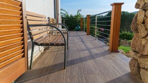 A wooden bench on a balcony with a metal railing, a stone wall, and a view of greenery. - Petra manna summer Palau Sardinia  (PALAU)
