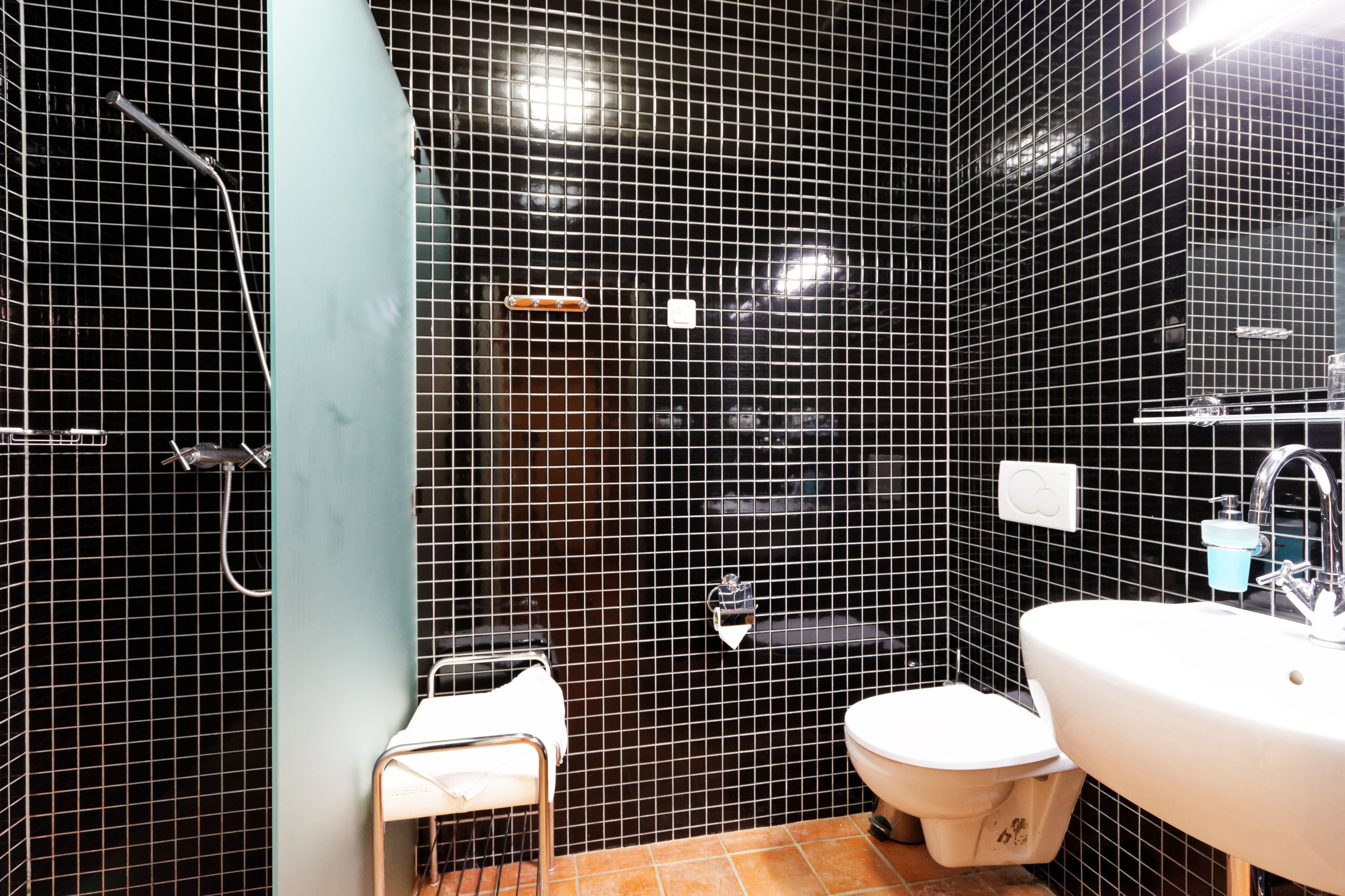 A bathroom with black tiled walls, a white sink, a toilet, and a shower area.