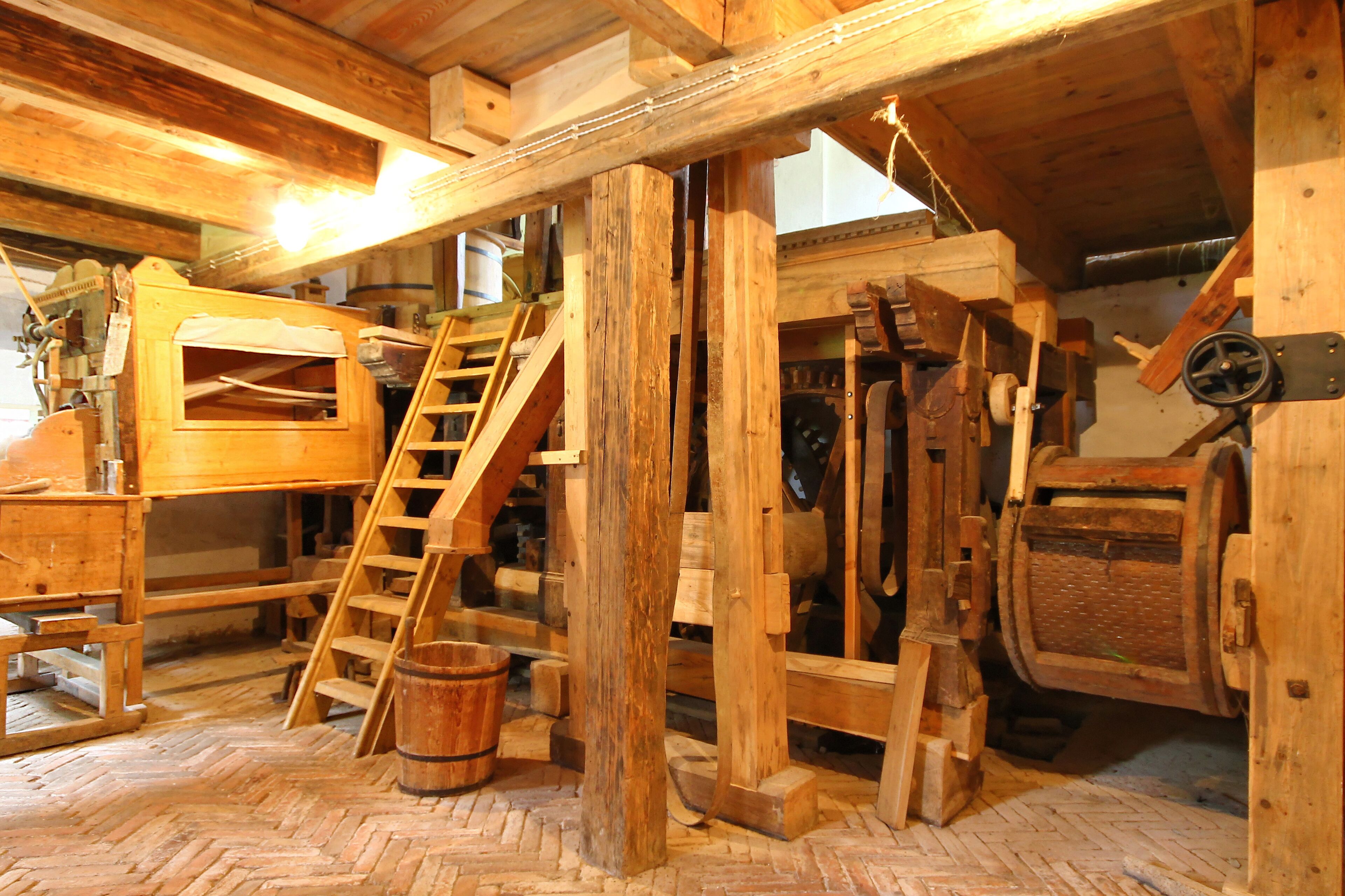 A rustic wooden interior with a wooden staircase, a large wooden machine, and a wooden table.